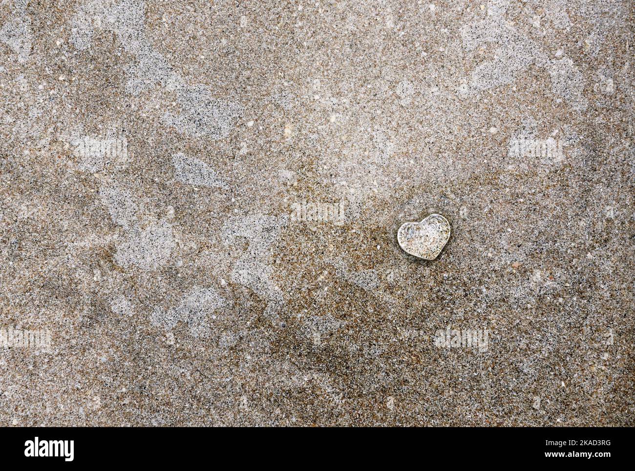 Piccolo cuore di vetro chiaro sulla spiaggia di sabbia con sottile strato d'acqua. Foto Stock