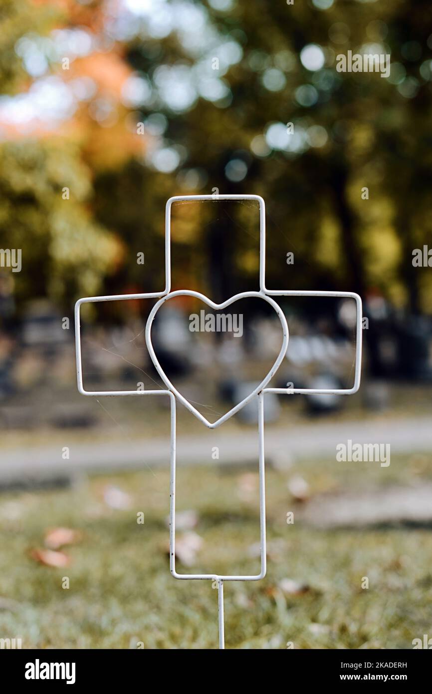 Croce di filo con un marcatore di tomba di cuore in un cimitero in autunno. Lapide del bambino in autunno. Foto Stock Croce di filo con un marcatore di tomba di cuore in un cimitero in autunno. Lapide del bambino in autunno. Foto Stock