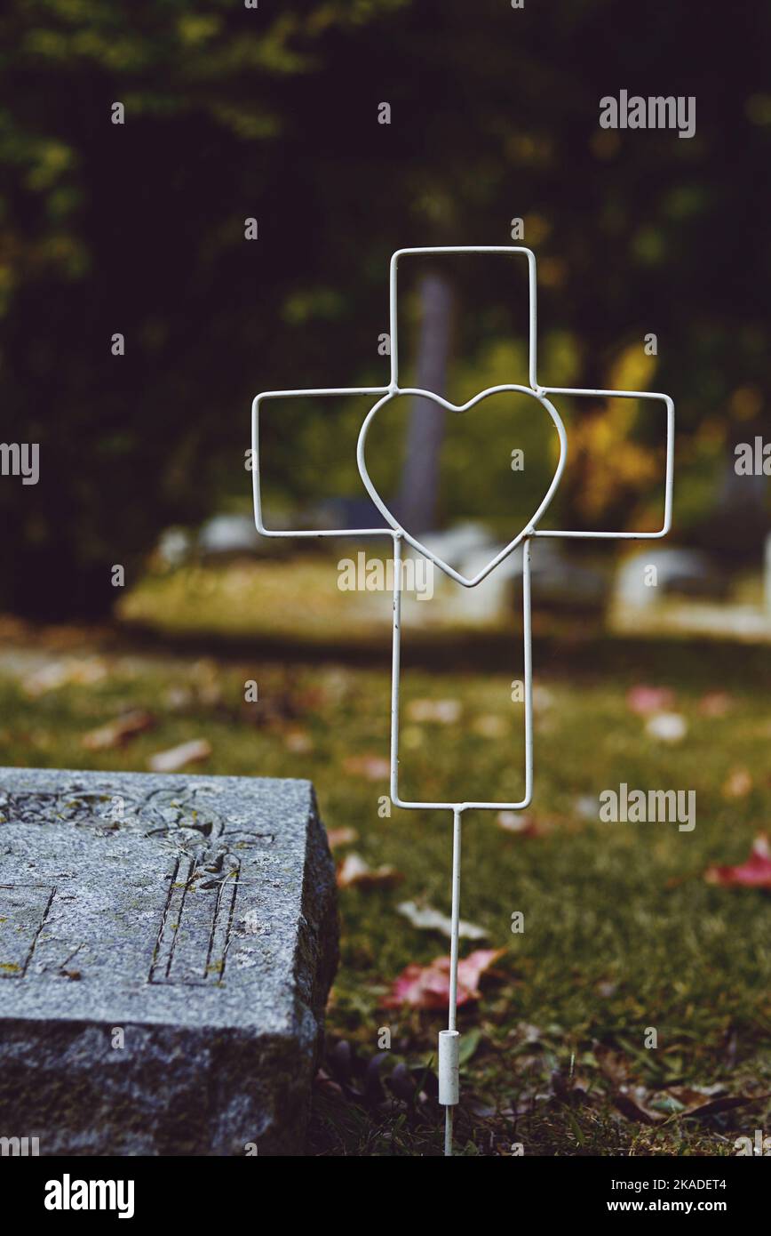 Croce di filo con un marcatore di tomba di cuore in un cimitero in autunno. Lapide del bambino in autunno. Foto Stock Croce di filo con un marcatore di tomba di cuore in un cimitero in autunno. Lapide del bambino in autunno. Foto Stock