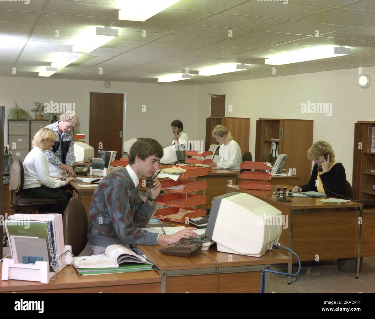 1990, uffici storici a pianta aperta, dipendenti maschi e femmine che lavorano alle scrivanie, alcuni al telefono e che utilizzano terminali informatici dell'epoca, Inghilterra, Regno Unito. Foto Stock