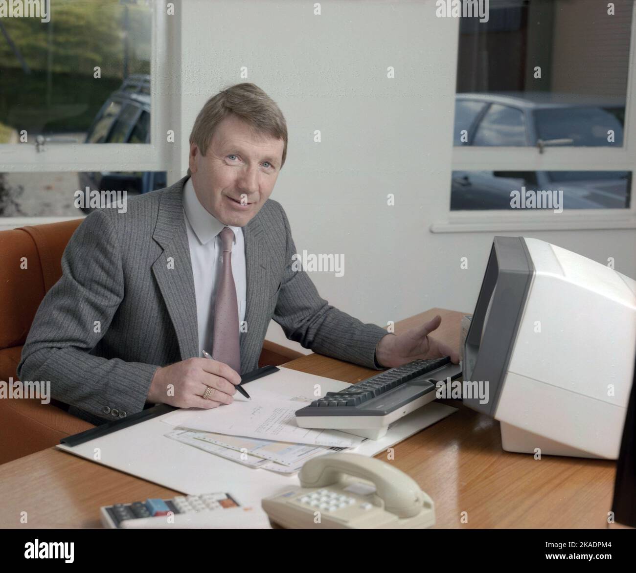 1989, storico, dirigente aziendale senior nel suo ufficio, seduto su una scrivania con penna e carta su un desktop blotter e un piccolo computer terminale e tastiera dell'epoca, Inghilterra, Regno Unito. Foto Stock