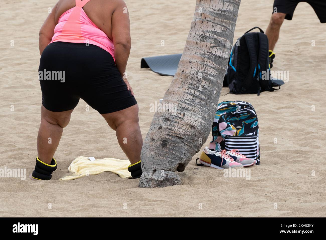 Donna obesa con pesi alle caviglie che si esercita sulla spiaggia in Spagna Foto Stock