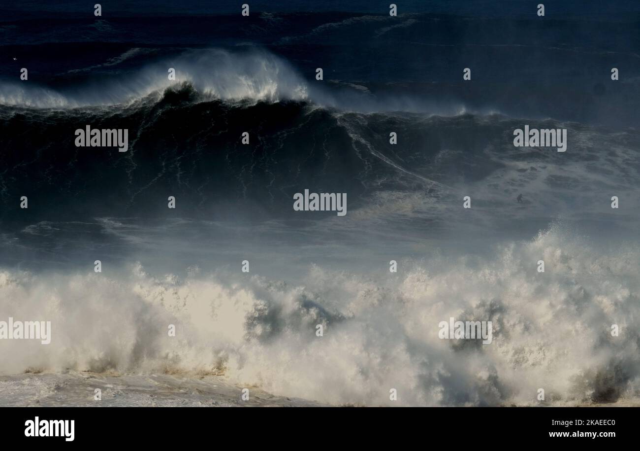 Un surfista temerario cavalca un'onda gigante in una competizione di surf a Nazaré, Portogallo. La grande stagione delle onde a Nazare è da ottobre a marzo Foto Stock