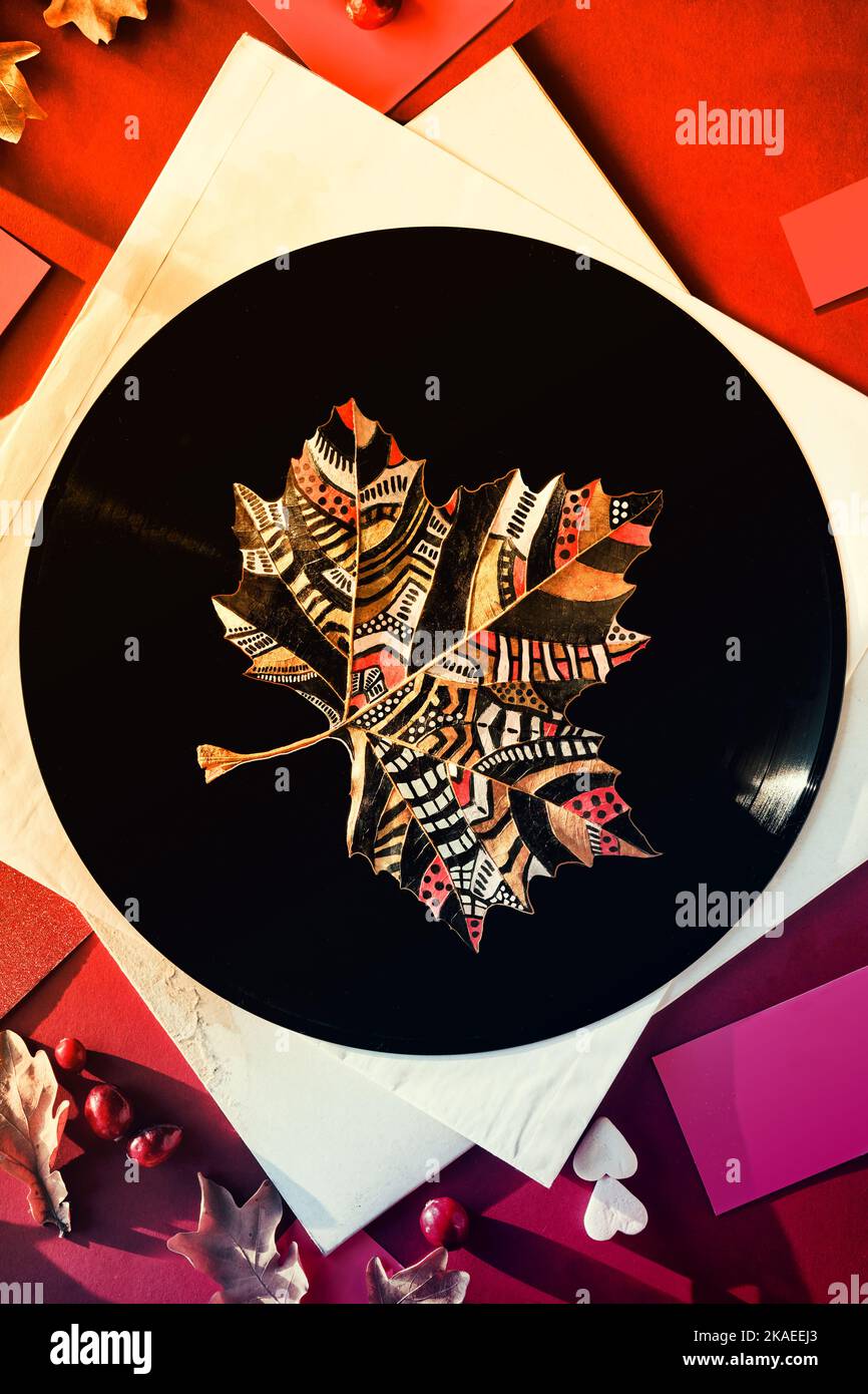 Leaf Art, dipinto foglia di sicomoro a secco autunnale su vinile vintage record e maniche di carta su sfondo arancione, carta magenta con decorazione autunnale. Foto Stock