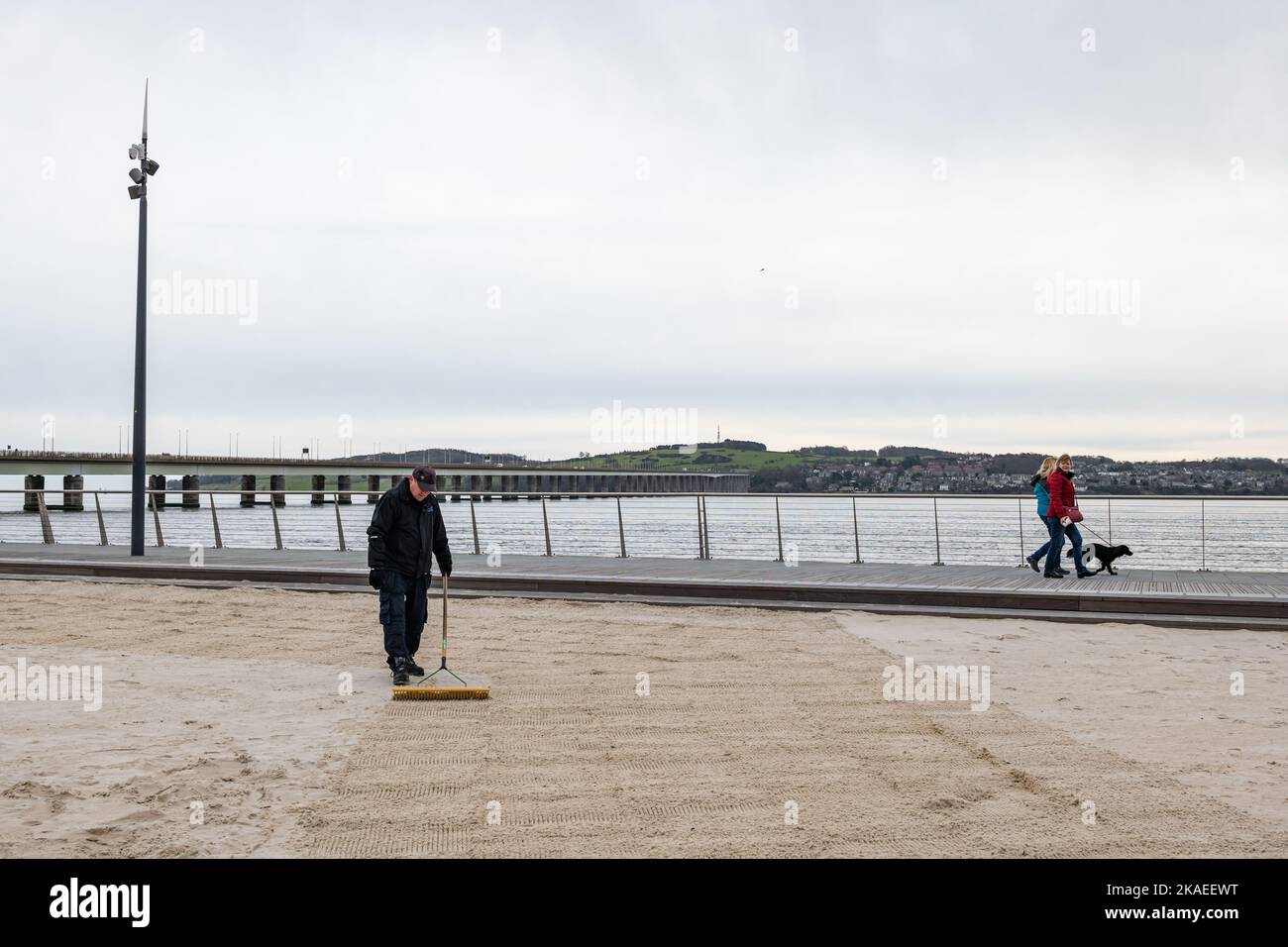 Addetto alla manutenzione che rastrellano sabbia sulla spiaggia urbana, Dundee Waterfront o Esplanade di River Tay, Scotland, UK Foto Stock