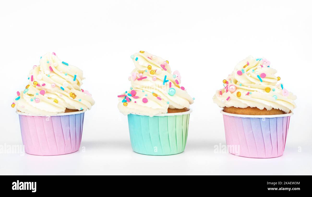Cupcake alla vaniglia in tazzine di carta sfumata. Graziosi cupcake con crema di burro, decorati con coloratissimi spruzzi su sfondo bianco. Festa a Foto Stock