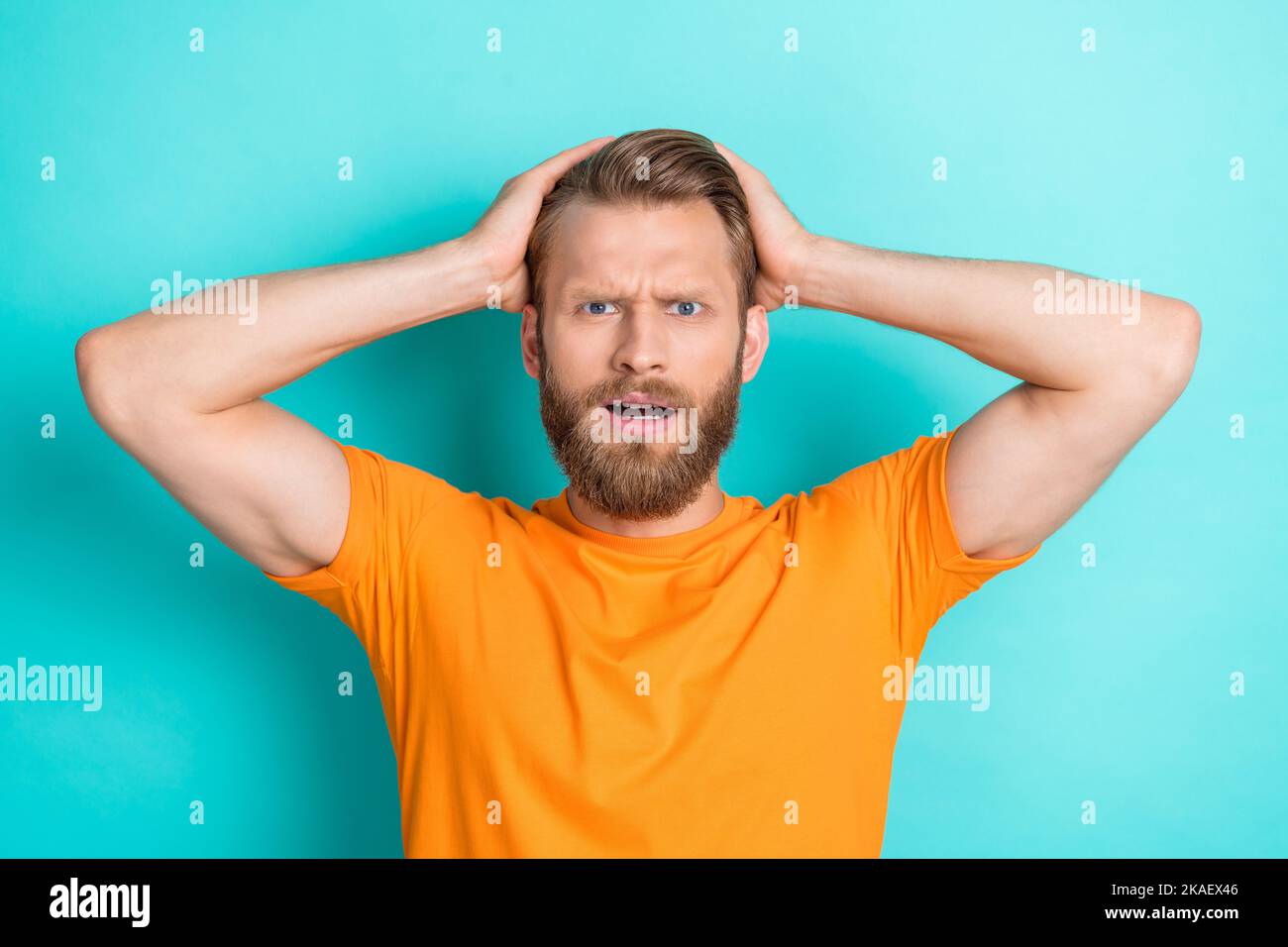 Foto dell'uomo stressante e infelice con i capelli biondi, le braccia della maglietta arancione vestite sulla testa fissando isolato su sfondo di colore teal Foto Stock