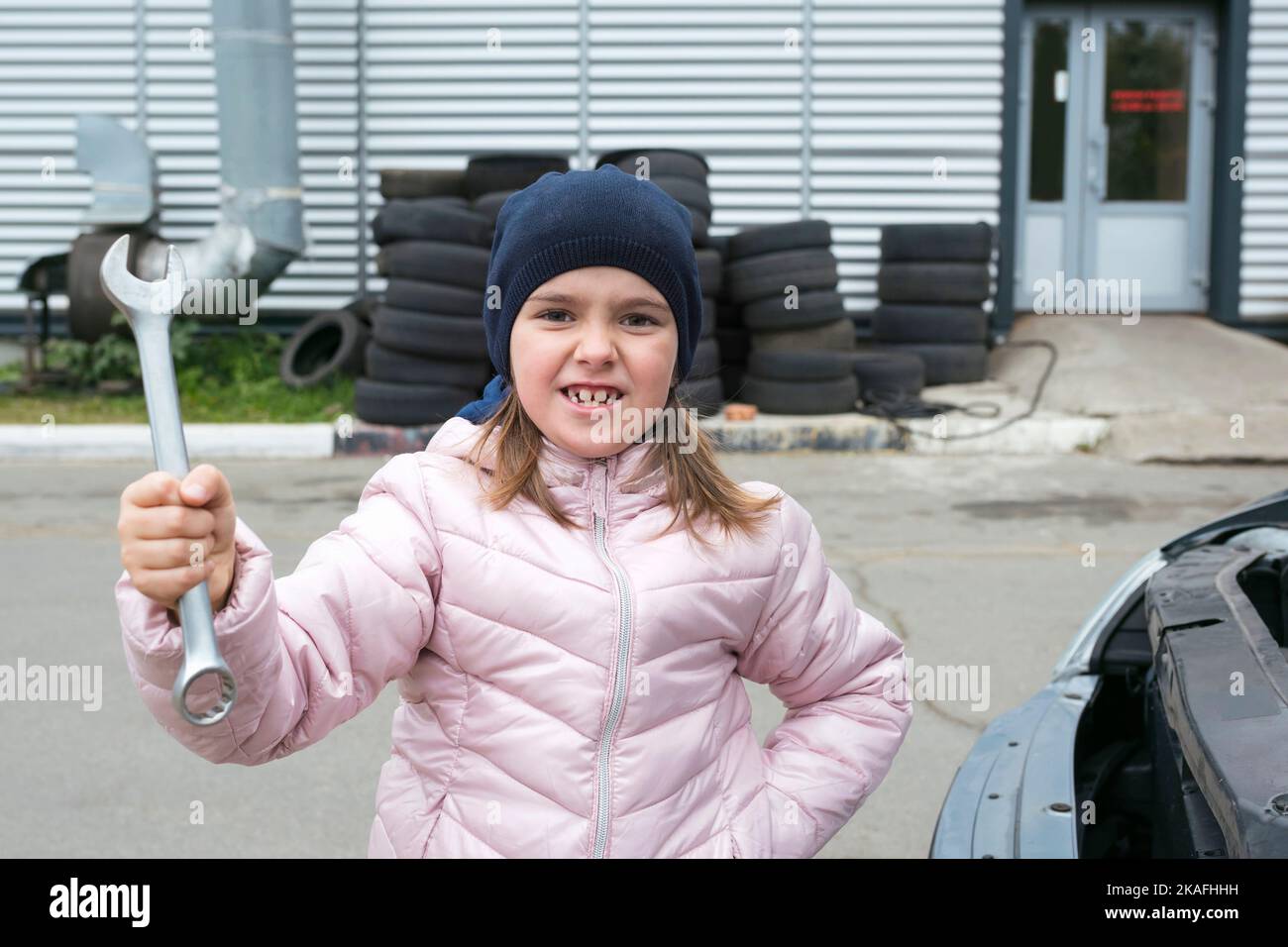 Ritratto di una bambina con chiave sullo sfondo di un servizio auto. Meccanico auto per bambini. Concetto di Servizio di Riparazione dell'automobile Foto Stock