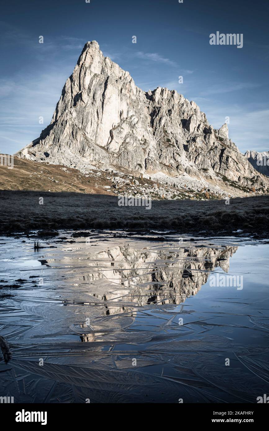 La parete rocciosa del Monte Ragusela si riflette nell'acqua e nel ghiaccio di uno stagno in una gelida mattinata autunnale al Passo di Giau, Dolomiti, Italia Foto Stock