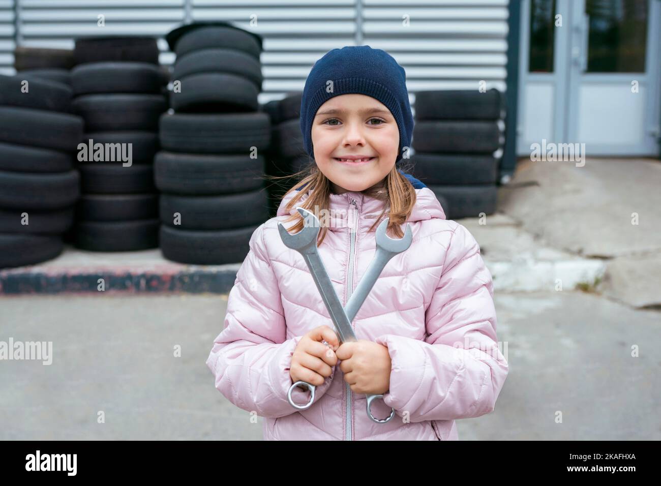 Ritratto di un bambino felice con chiavi sullo sfondo di un garage e pneumatici ruote e veicolo di servizio. Concetto di riparazione automatica Foto Stock