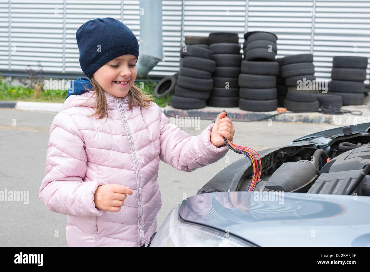 Ragazza piccola felice che ripara un elettricista in un'automobile. Servizio auto Foto Stock