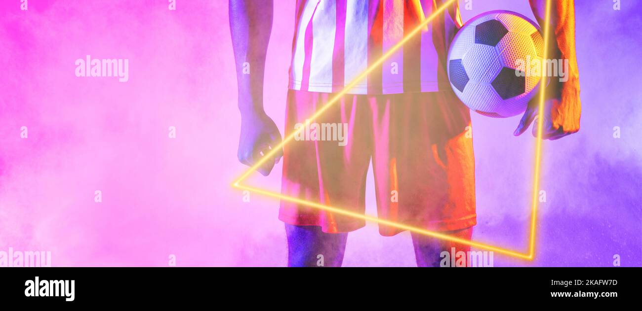 Sezione centrale del giocatore maschio afro-americano che tiene il pallone con la forma triangolare illuminata sopra il fumo Foto Stock