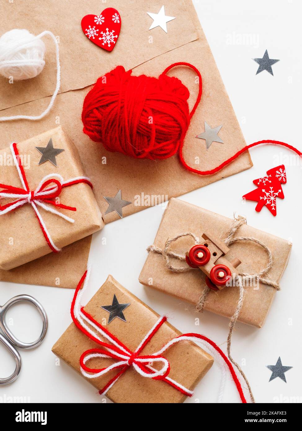 Natale e Capodanno regali fai-da-te in carta artigianale. Regali di festa legati con fili bianchi e rossi con trenino giocattolo e simbolo del cuore rosso come decorazione. Foto Stock