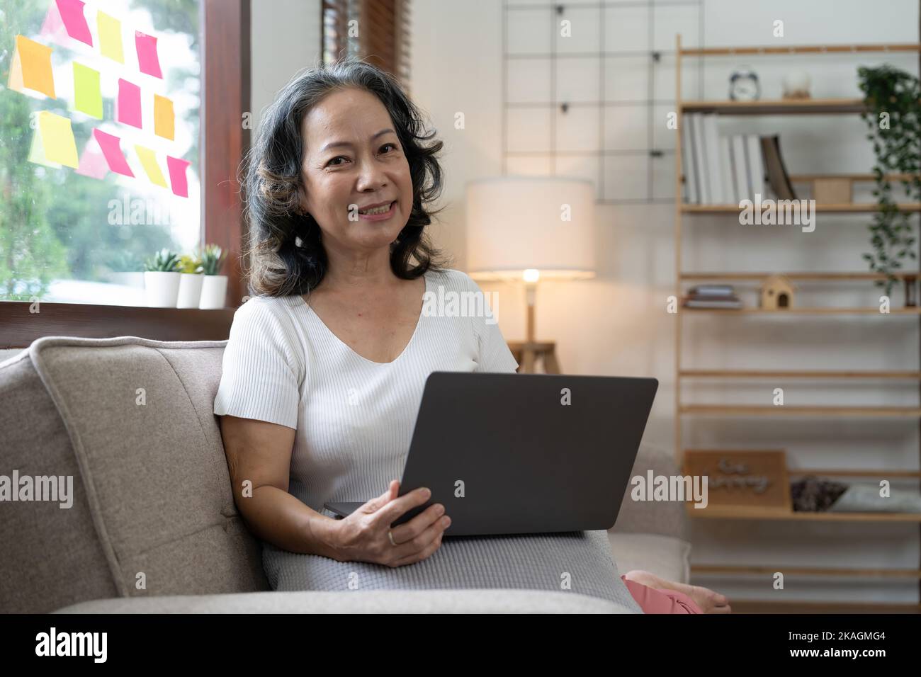 Ritratto di donna asiatica anziana felice guardando la macchina fotografica a casa. Vecchia donna di successo che lavora a casa. Bella donna anziana elegante sorridente e. Foto Stock