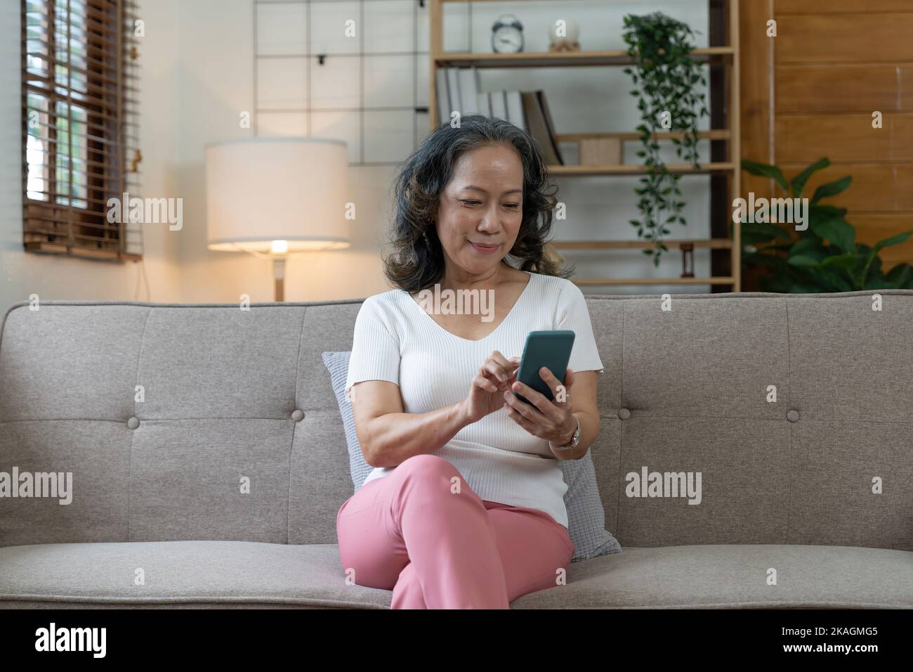 Donna anziana sorridente che usa il suo smartphone, si connette online e utilizza le app a casa Foto Stock