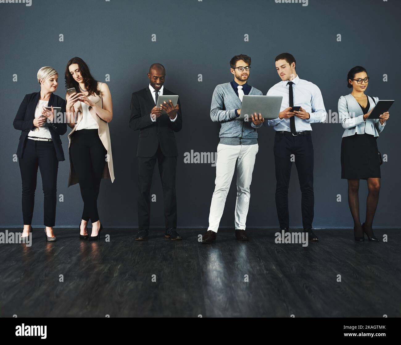 Theyve tutti hanno ottenuto i sensi astuti fare il commercio. Studio di un gruppo di uomini d'affari che utilizzano vari dispositivi digitali su uno sfondo grigio. Foto Stock