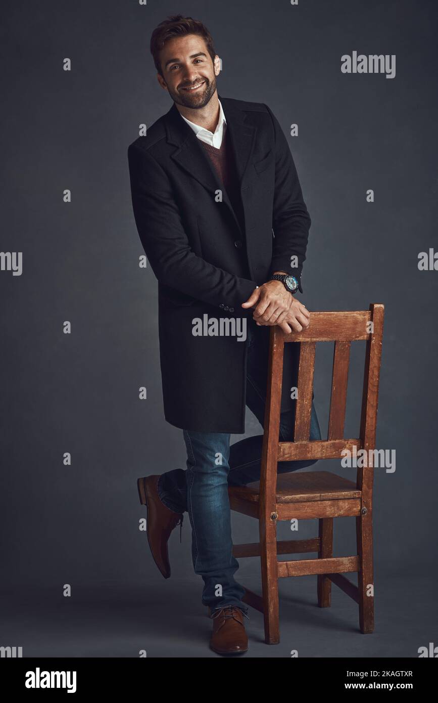 Chi ha detto casual cant essere elegante. Studio ritratto di un giovane uomo elegantemente vestito in piedi accanto a una sedia su uno sfondo grigio. Foto Stock