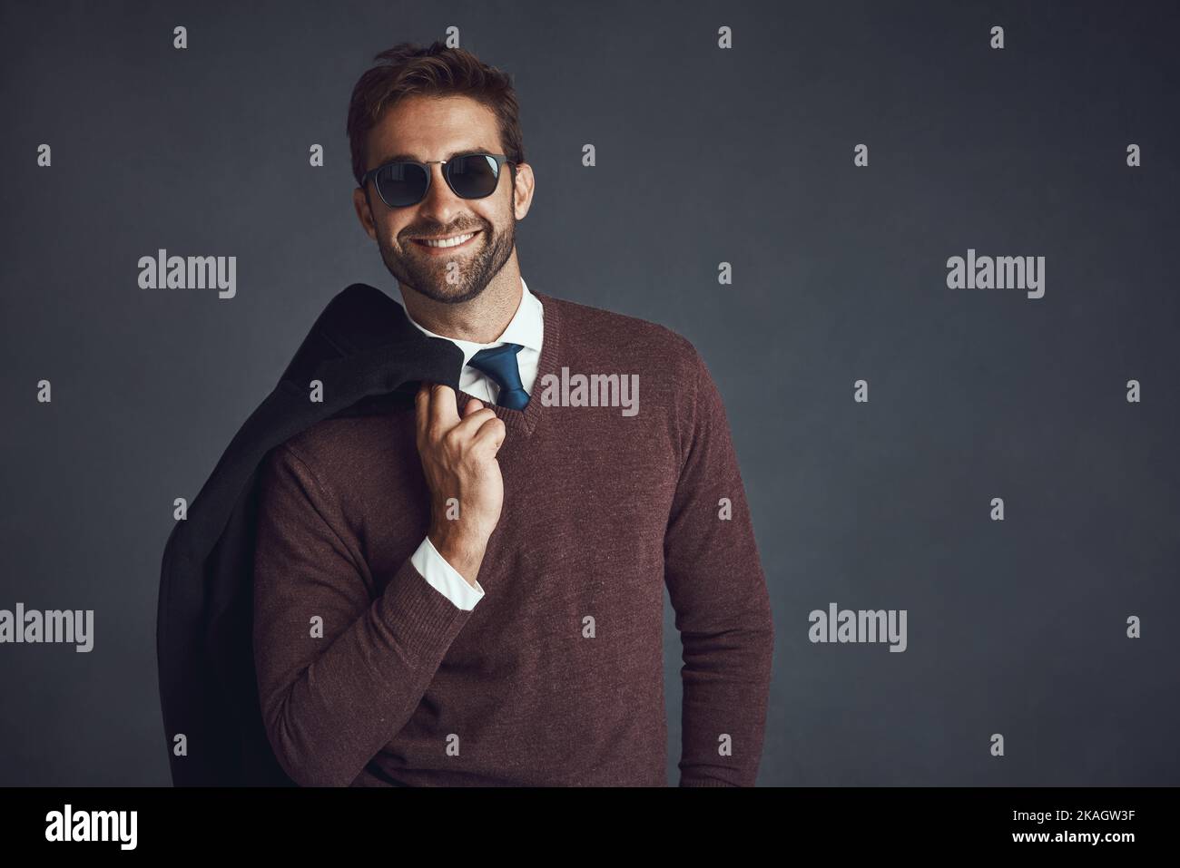 Fa tutto lo stile osservare buono. Studio ritratto di un giovane uomo elegantemente vestito che porta la sua giacca su uno sfondo grigio. Foto Stock