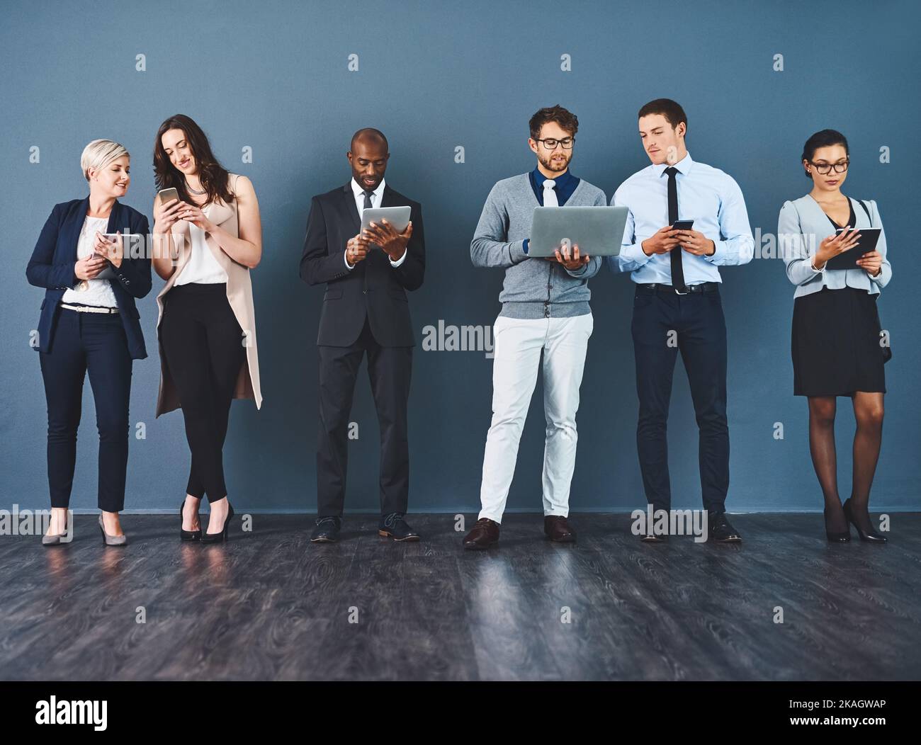Theyve tutti hanno ottenuto i sensi astuti fare il commercio. Studio di un gruppo di uomini d'affari che utilizzano vari dispositivi digitali su uno sfondo grigio. Foto Stock