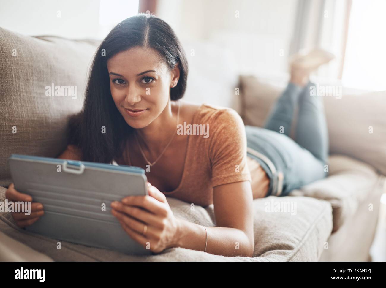 Intrattenimento con i divani in formato digitale. Una giovane donna che si rilassa e usa un tablet digitale sul divano di casa. Foto Stock