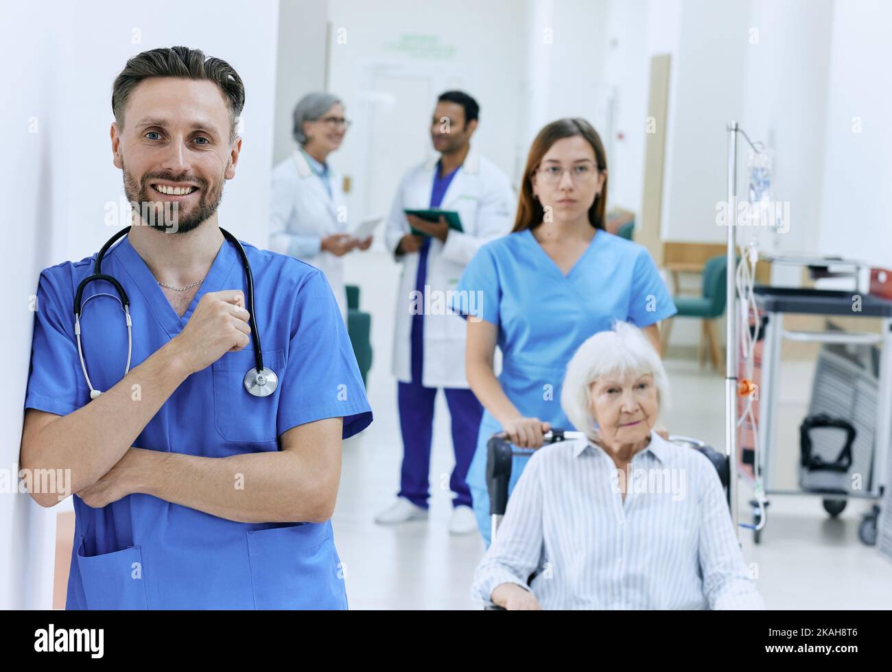 Ritratto del tecnico medico con stetoscopio in piedi davanti al corridoio dell'ospedale con personale medico funzionante. occupazione medica Foto Stock