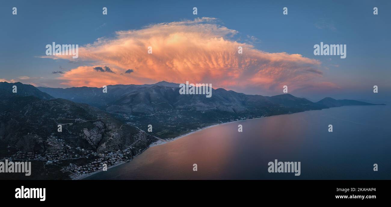 Paesaggio costiero panoramico, vista aerea serale della Riviera albanese contro un cielo spettacolare. Spiaggia, montagne, nuvola di tempesta illuminata rosa. Somma Foto Stock