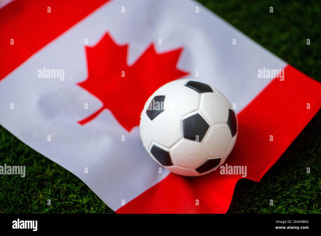 Nazionale di calcio del Canada. Bandiera nazionale su erba verde e palla da calcio. Carta da parati da calcio per Campionato e Torneo nel 2022. Internazionale del mondo Foto Stock