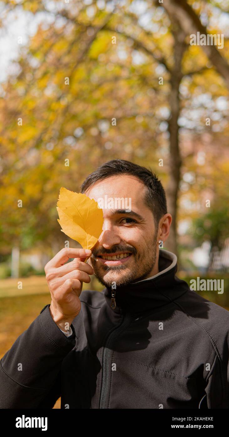 Uomo sorridente in piedi nel parco con una foglia gialla autunnale davanti al suo volto, Provincia di Leon, Spagna Foto Stock