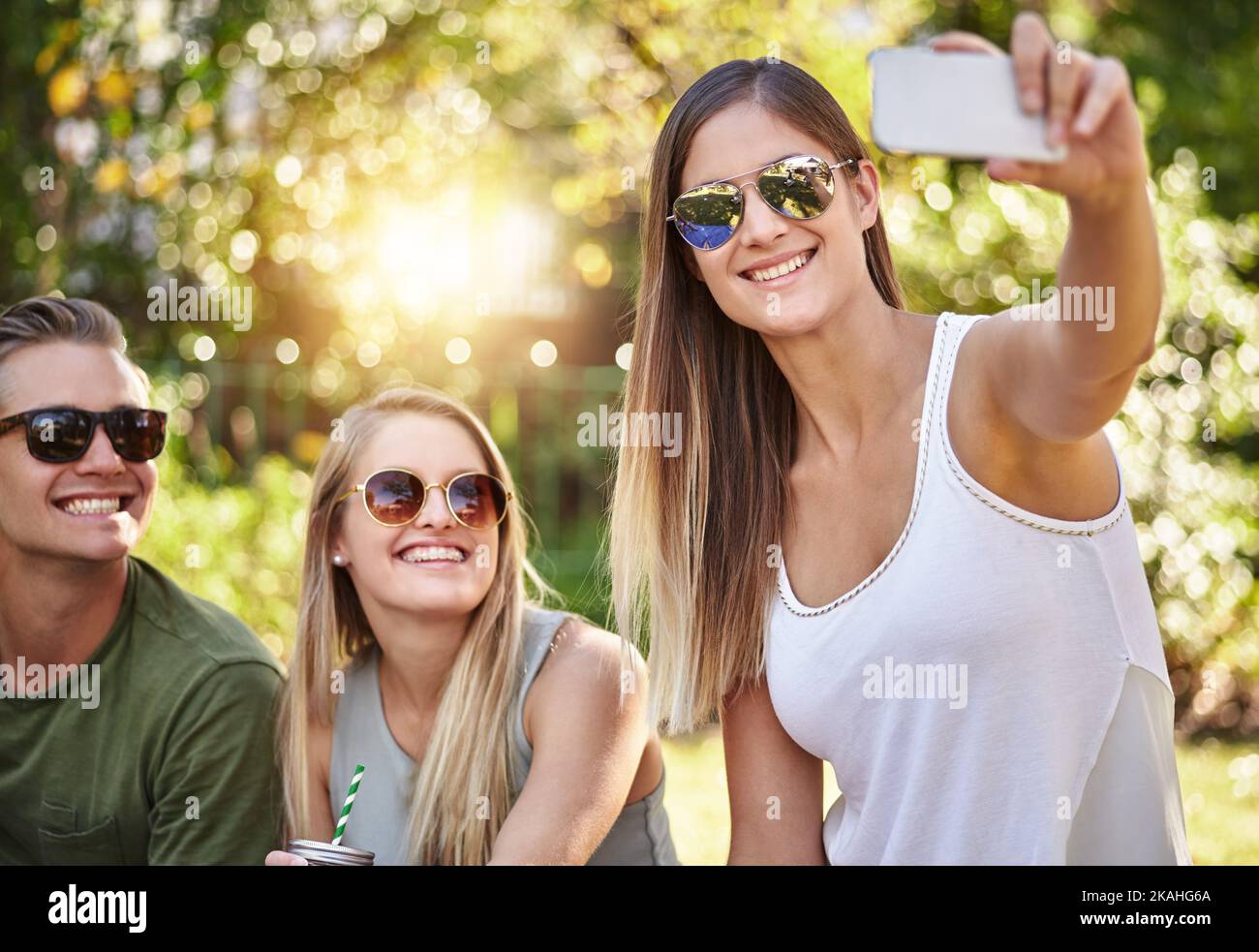 Sorridi. Un giovane gruppo di amici che scattano selfie mentre sorseggi qualche drink al sole estivo. Foto Stock