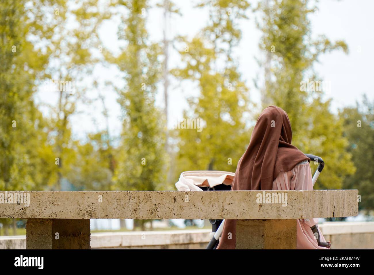 mommia musulmana velata sulla schiena con il suo bambino nel parco. Migrazione in Spagna Foto Stock
