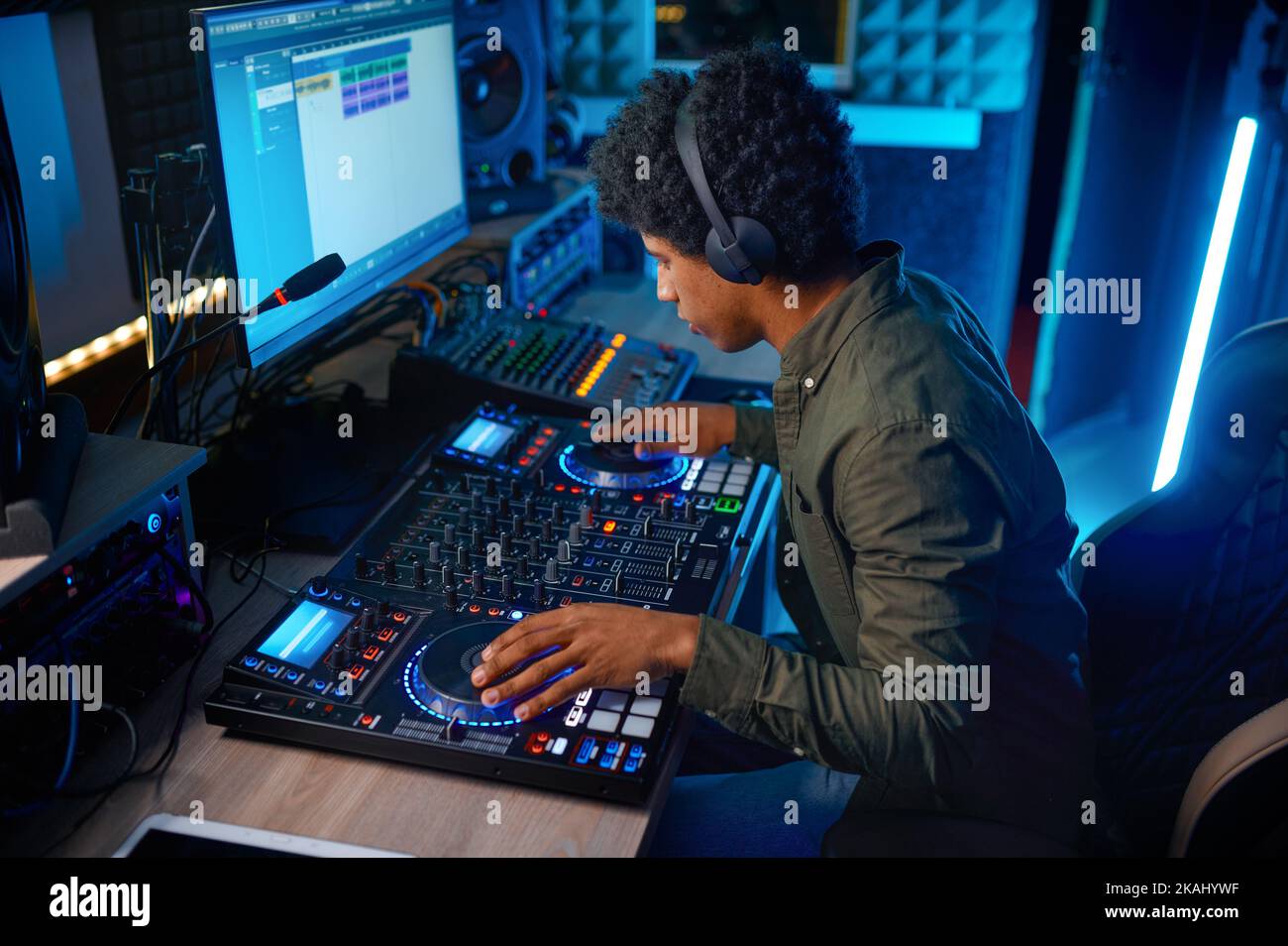 Giovane uomo che paga musica sul mixer audio nella stazione radio Foto Stock