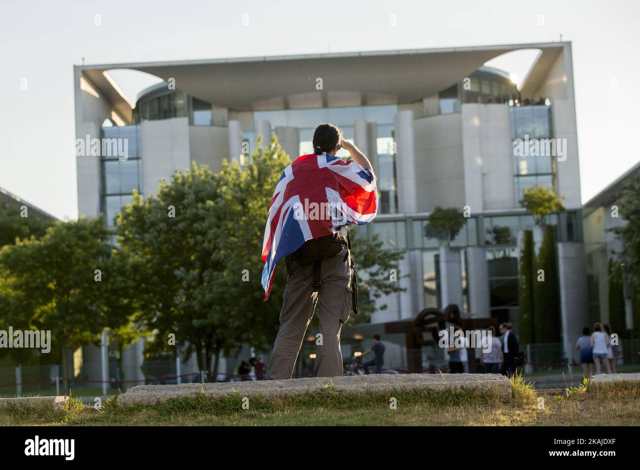 Un uomo che indossa la bandiera britannica Union Jack guarda alla Cancelleria mentre la cancelliera tedesca Angela Merkel e il primo ministro britannico Theresa May si incontrano a Berlino, in Germania, il 20 luglio 2016. Foto Stock