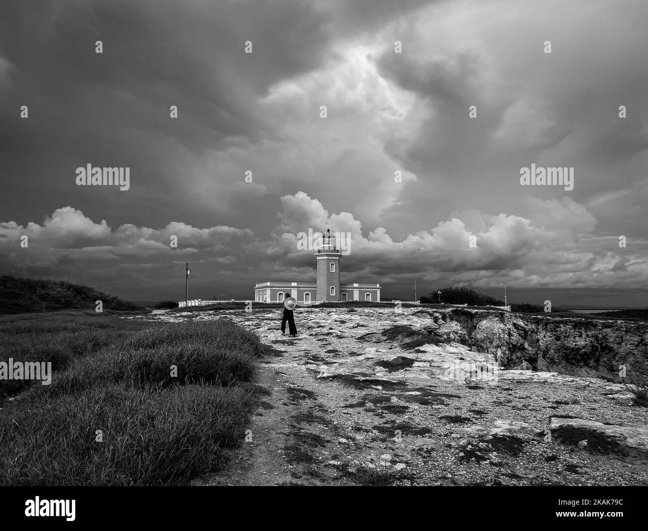 Una vista in scala di grigi di un uomo che cammina verso il Faro Los Morrillos sotto il cielo nuvoloso Foto Stock