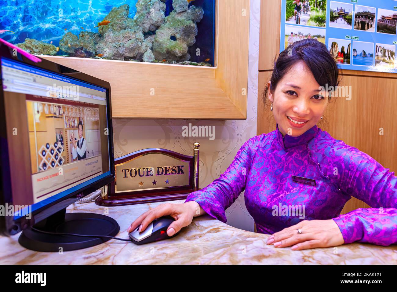 L'addetto alla reception dell'hotel vietnamita indossa ao dai e prenota su internet al banco escursioni, ho Chi Minh City, Vietnam Foto Stock