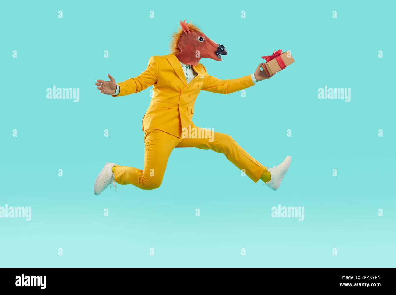 Uomo in divertente maschera cavallo tenendo presente, correndo veloce e saltando su sfondo blu Foto Stock