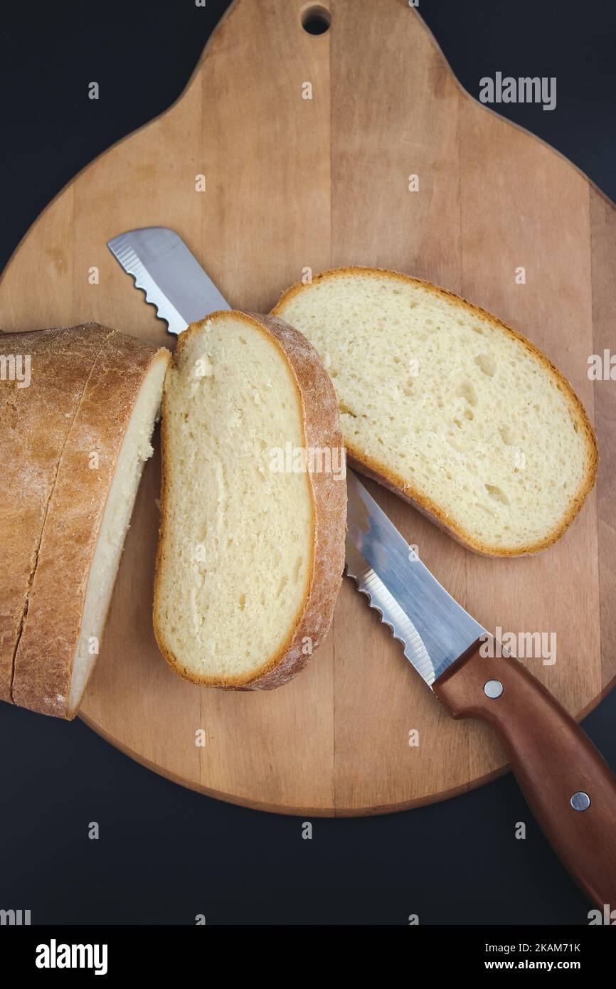 Pane appena sfornato, affettato con un coltello seghettato su un tagliere di legno. Foto Stock