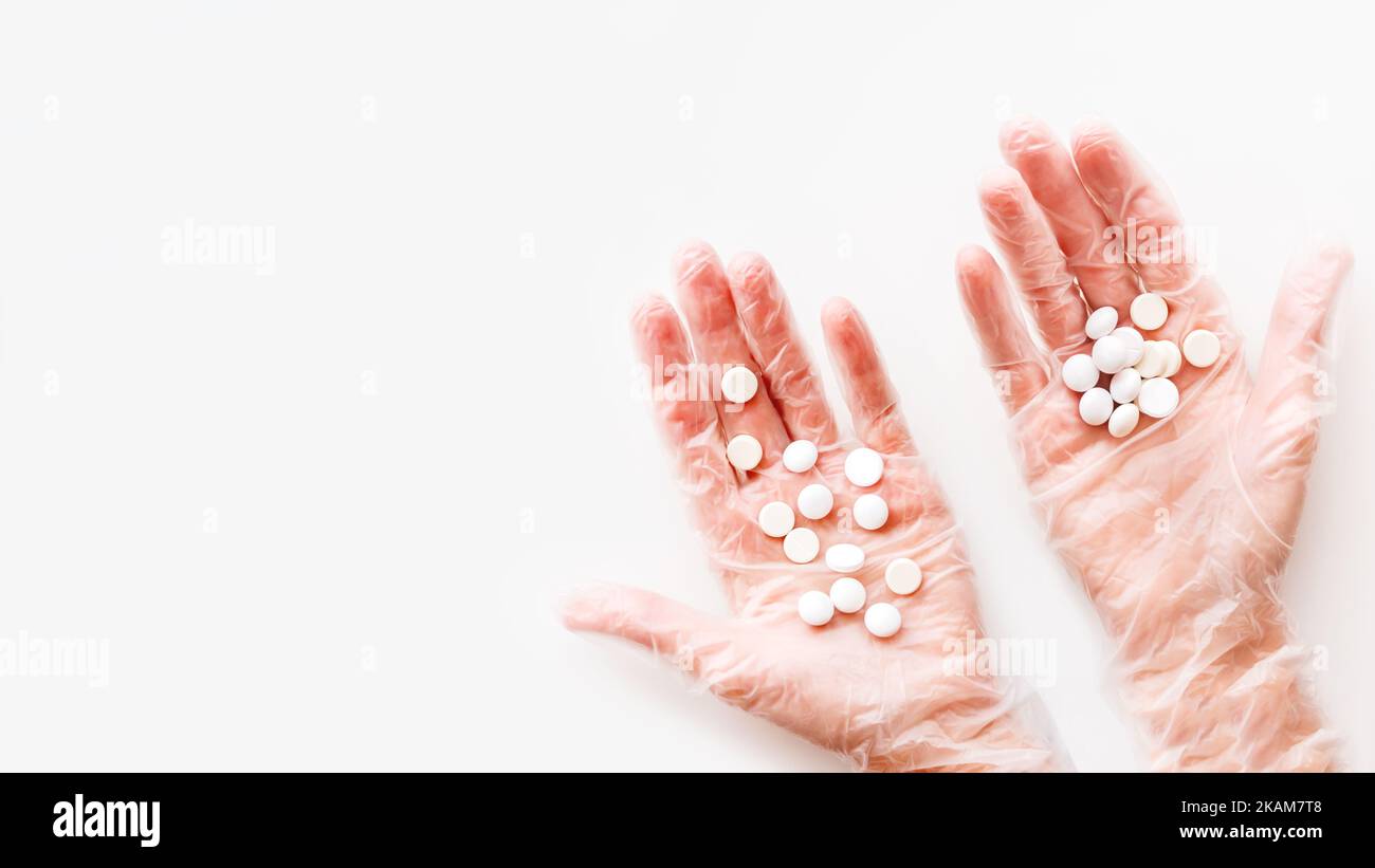 Mani del palmo del medico in guanti protettivi trasparenti pieni di pillole bianche. Capsule con medicinali su sfondo bianco con spazio di copia. Piatto Foto Stock