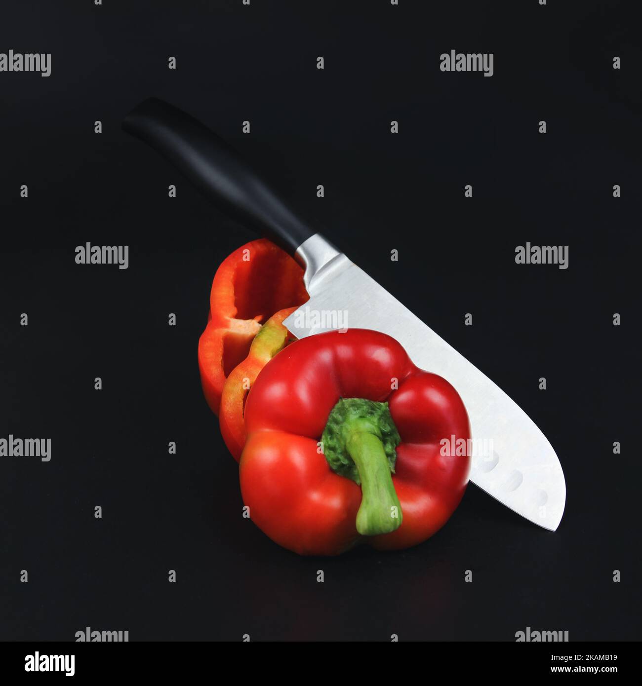 Un coltello affilato e un pepe su fondo nero su superficie nera. Pepe da giardino fresco maturo e coltello Foto Stock