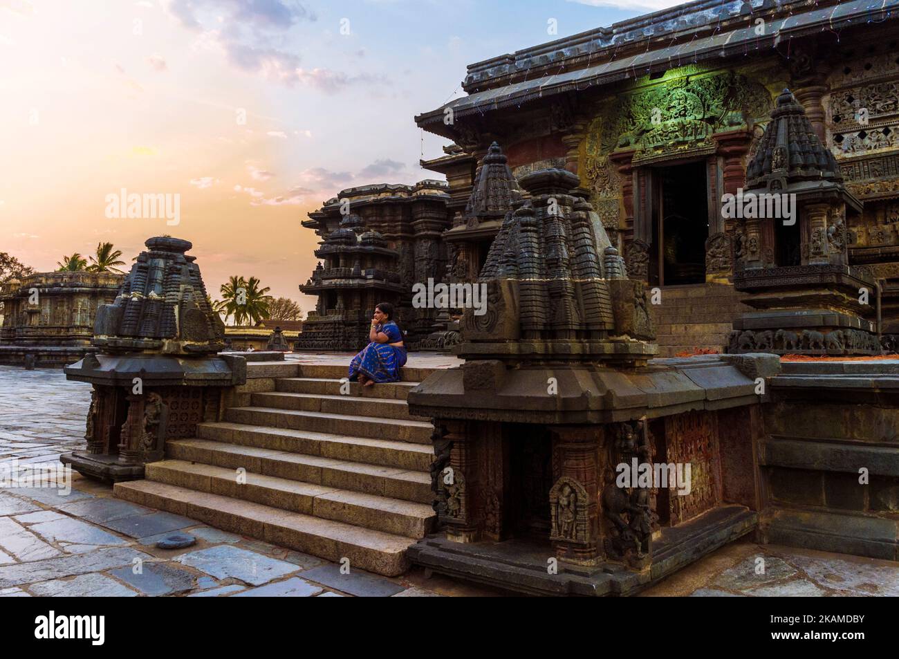 Belur, Karnataka, India: 12th ° secolo Channakeshava Tempio al tramonto. Una donna siede sui gradini del Tempio principale di Kesava. Foto Stock