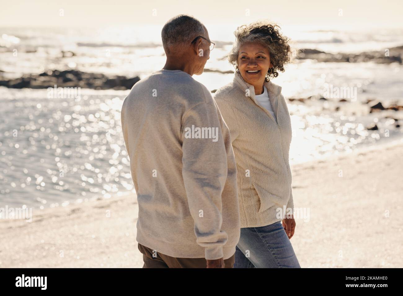 Allegra coppia anziana sorridente l'una all'altra mentre si cammina lungo la spiaggia. Coppia anziana romantica che passa un certo tempo di qualità insieme dopo re Foto Stock