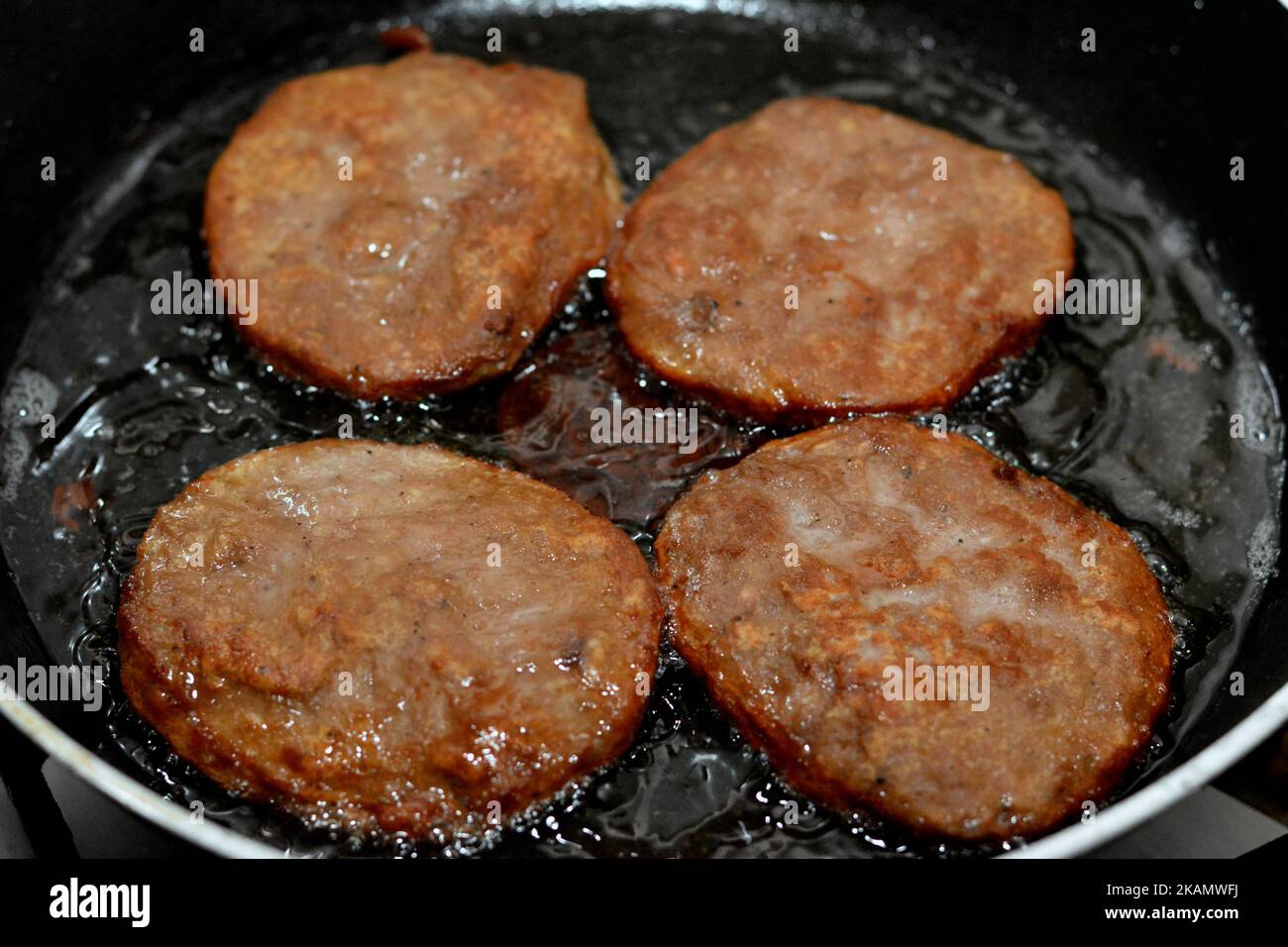 Un primo piano di 4 pezzi di hamburger di manzo fritto piccante cucinato in un olio bollente poco profondo in una padella antiaderente, Fast food, Junk food Concept, FAST fatto in casa Foto Stock