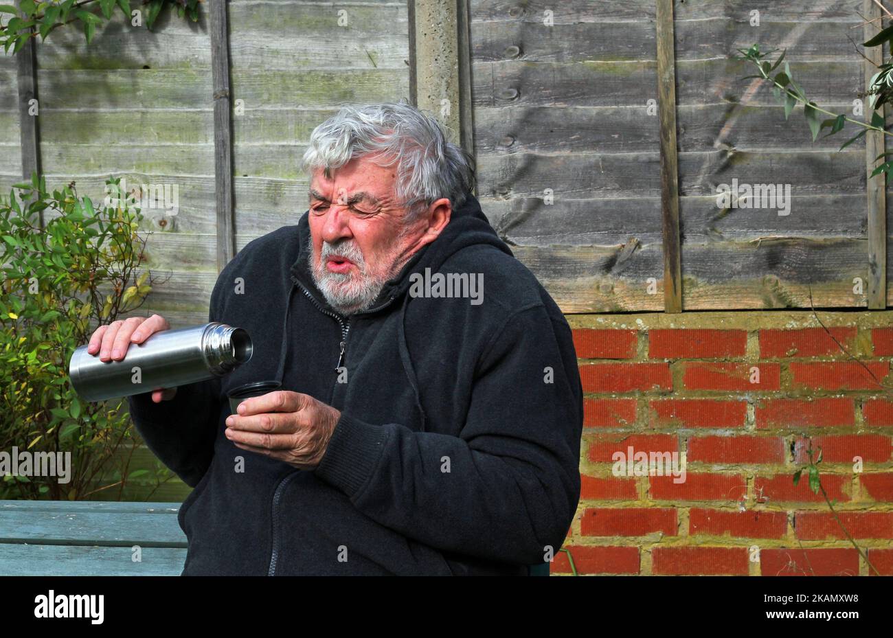 Uomo con un pallone da vuoto thermos che offre una tazza di caffè o tè. Guardando verso la fotocamera. Foto Stock