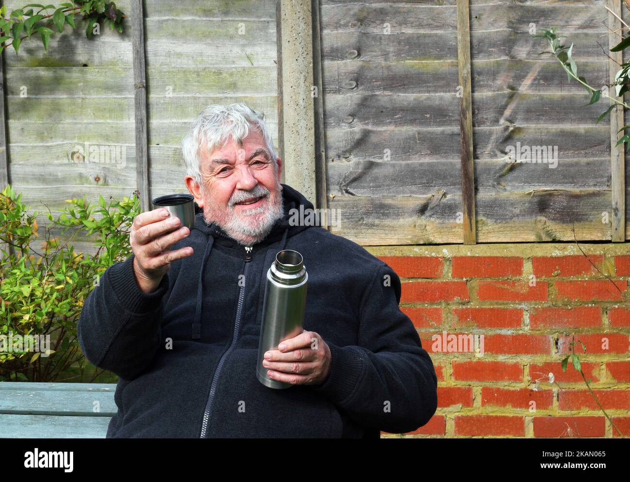 Uomo con un pallone da vuoto thermos che offre una tazza di caffè o tè. Guardando verso la fotocamera. Foto Stock
