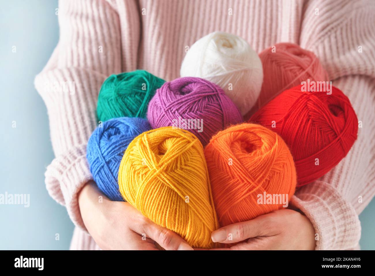 Donna che detiene filati di lana colorati o multicolore su sfondo blu. Molte sfere multicolore di fili primo piano. Concetto di lavorazione a maglia o a cucito. Foto Stock