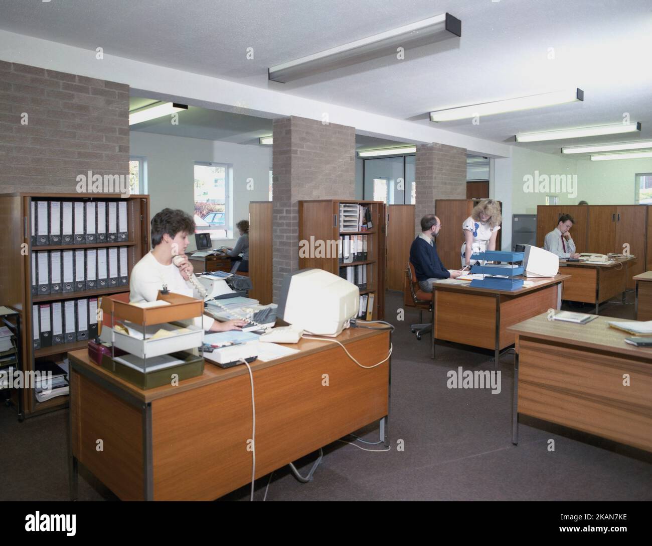 1989, personale storico, maschile e femminile che lavora in un ufficio, seduto a scrivanie di legno, con in vassoi, aggiungendo macchine e piccoli terminali informatici del giorno. Foto Stock