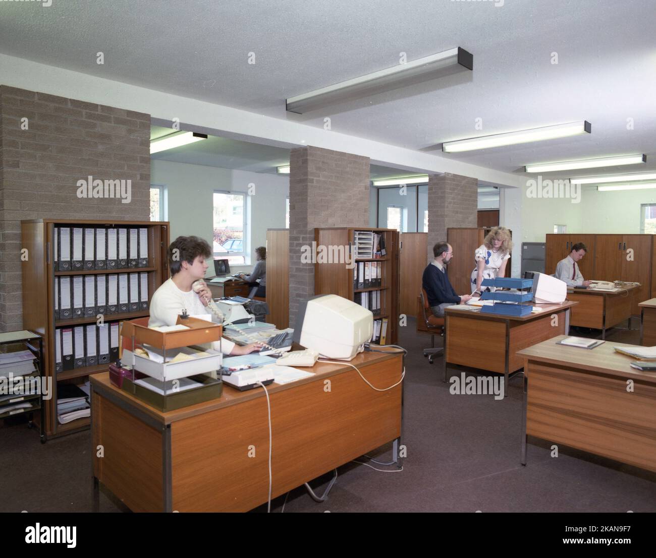 1989, personale storico, maschile e femminile che lavora in un ufficio, seduto a scrivanie di legno, con in vassoi, aggiungendo macchine e piccoli terminali informatici del giorno. Foto Stock