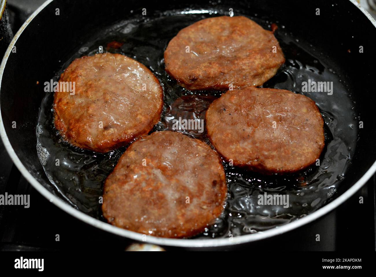 Un primo piano di 4 pezzi di hamburger di manzo fritto piccante cucinato in un olio bollente poco profondo in una padella antiaderente, Fast food, Junk food Concept, FAST fatto in casa Foto Stock