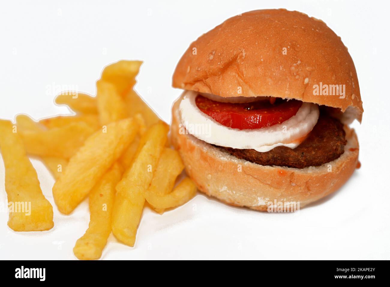 focus selettivo del panino hamburger di manzo con fette di anelli di cipolla e pomodori, con patatine fritte dita di patate isolate sul dorso bianco Foto Stock
