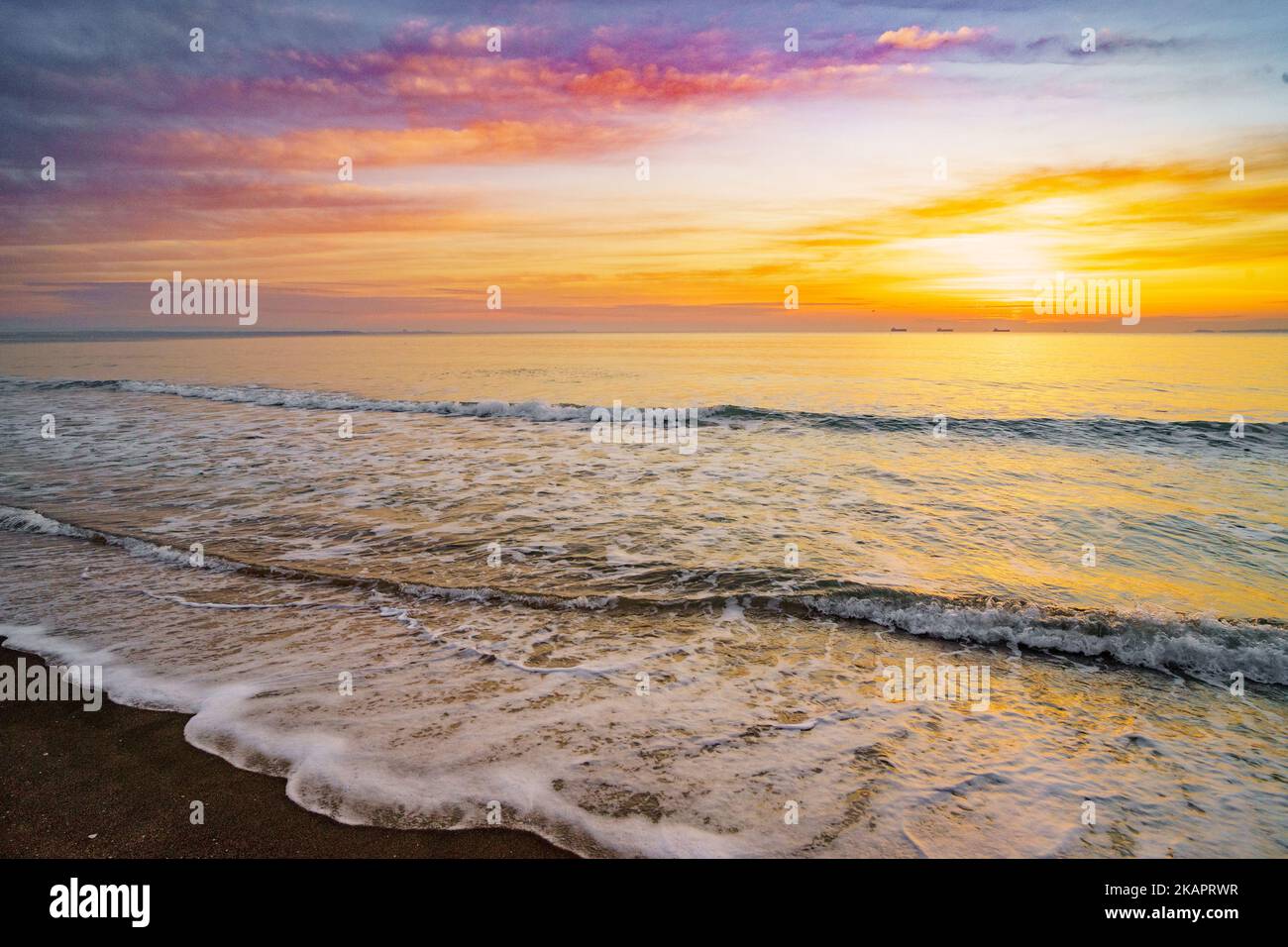 Una bella vista di un mare con piccole onde schiumose durante il tramonto arancione Foto Stock