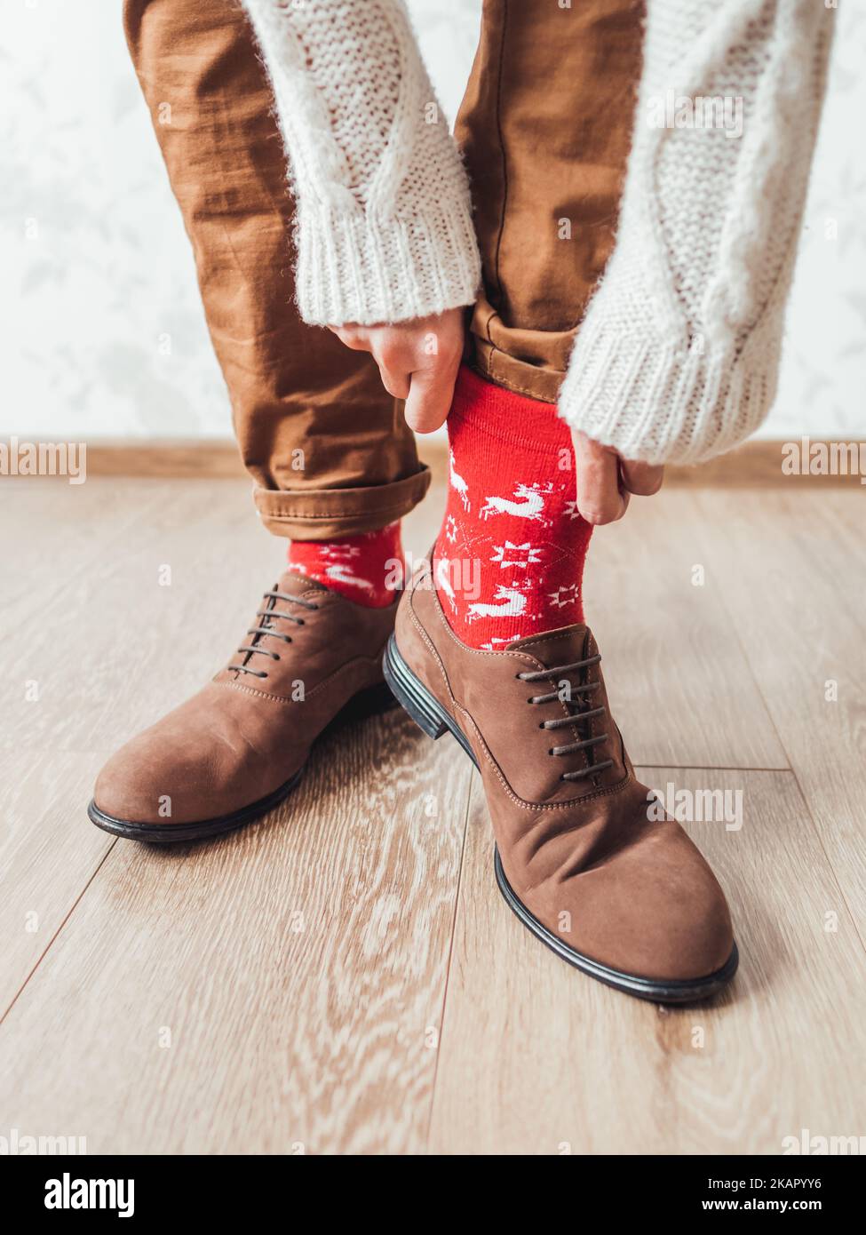 Il giovanotto tira la gamba dei pantaloni chino per mostrare calze rosse con le renne. Modello scandinavo. Outfit per le vacanze invernali. Foto Stock